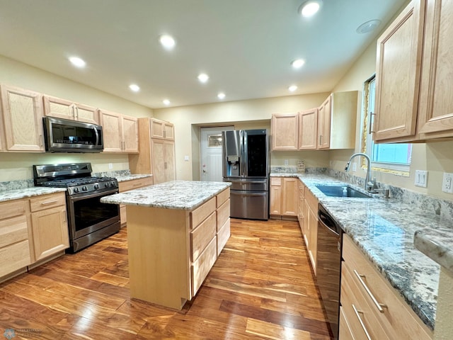 kitchen with light brown cabinetry, appliances with stainless steel finishes, sink, wood-type flooring, and a kitchen island