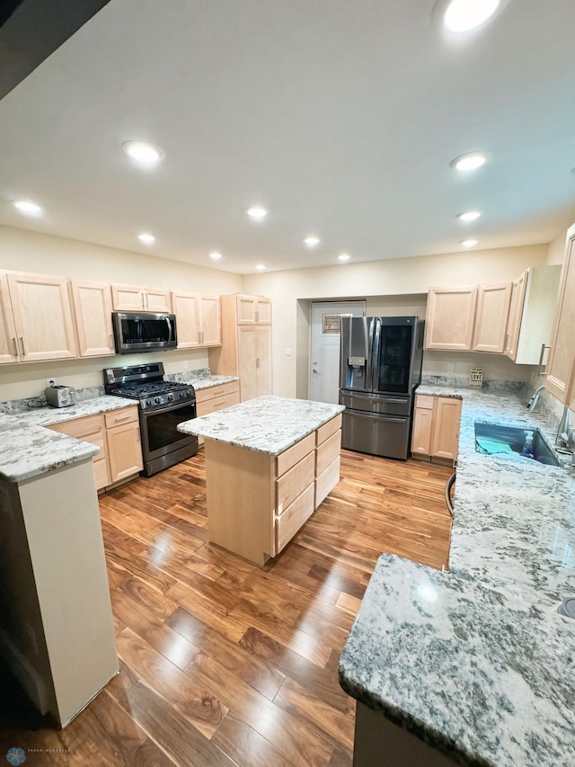 kitchen with a kitchen island, sink, light stone countertops, appliances with stainless steel finishes, and light hardwood / wood-style floors