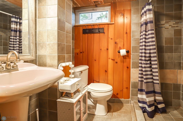 bathroom with a shower with shower curtain, tile patterned flooring, toilet, sink, and tile walls