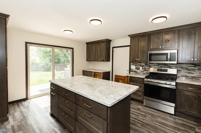 kitchen with dark hardwood / wood-style floors, dark brown cabinets, appliances with stainless steel finishes, tasteful backsplash, and a center island