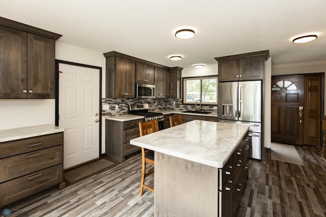 kitchen featuring dark hardwood / wood-style floors, appliances with stainless steel finishes, crown molding, a center island, and sink