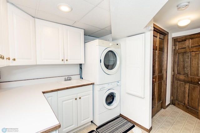 laundry area featuring stacked washer and clothes dryer, cabinets, sink, and light tile patterned floors