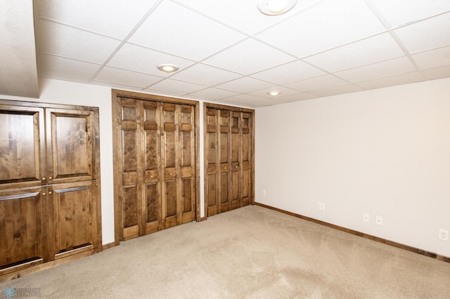 unfurnished bedroom with two closets, light colored carpet, and a drop ceiling