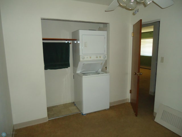 clothes washing area featuring stacked washer and clothes dryer, a baseboard heating unit, ceiling fan, and light colored carpet