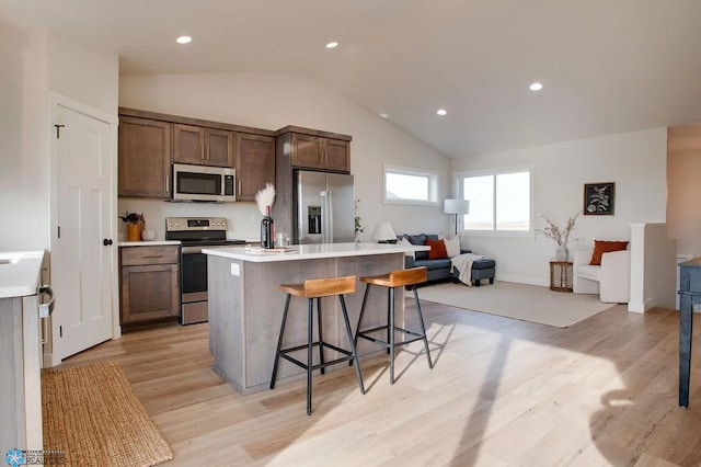 kitchen with lofted ceiling, a kitchen island with sink, stainless steel appliances, a kitchen breakfast bar, and light hardwood / wood-style floors