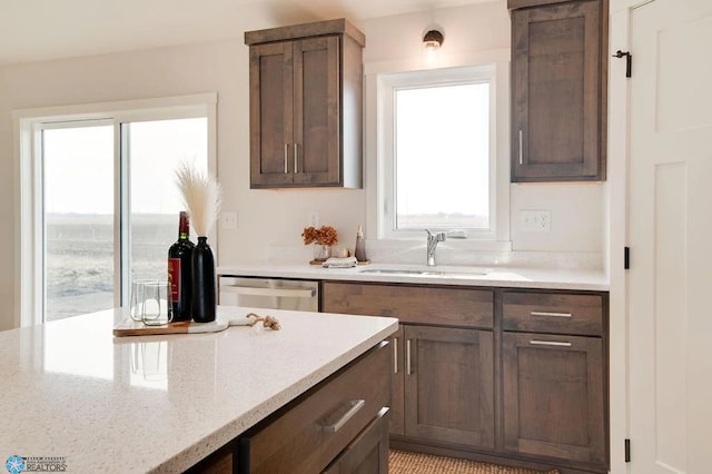 kitchen with dark brown cabinets, light stone countertops, stainless steel dishwasher, and sink