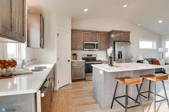 kitchen featuring vaulted ceiling, a breakfast bar, stainless steel appliances, light hardwood / wood-style flooring, and sink