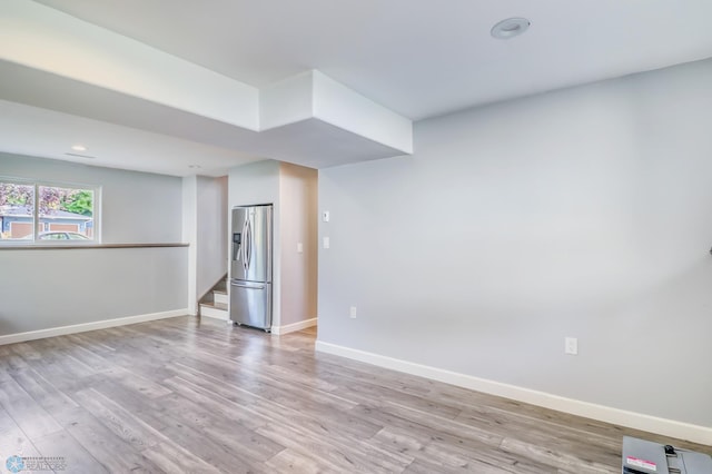 basement featuring light hardwood / wood-style floors and stainless steel fridge with ice dispenser