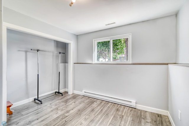 unfurnished bedroom featuring a baseboard radiator, light wood-type flooring, and a closet