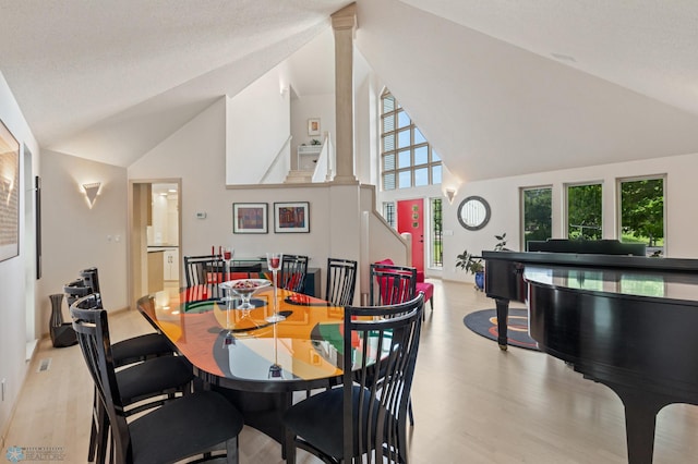 dining room with a textured ceiling, decorative columns, light hardwood / wood-style floors, and high vaulted ceiling