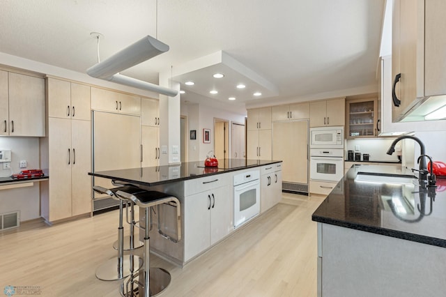 kitchen with dark stone counters, light wood-type flooring, a center island, built in appliances, and sink