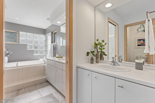 bathroom with a relaxing tiled tub, vanity, and a textured ceiling