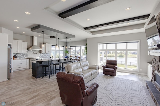 living room featuring a stone fireplace, beam ceiling, and light hardwood / wood-style floors