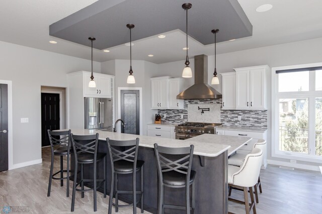 kitchen with stainless steel appliances, white cabinets, pendant lighting, wall chimney range hood, and a large island