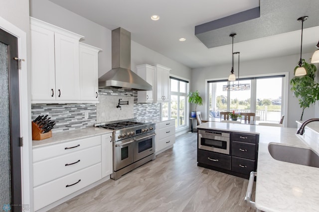 kitchen featuring wall chimney exhaust hood, pendant lighting, sink, white cabinets, and appliances with stainless steel finishes