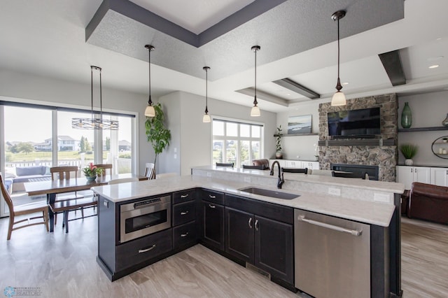 kitchen featuring a kitchen island with sink, a tray ceiling, decorative light fixtures, sink, and appliances with stainless steel finishes