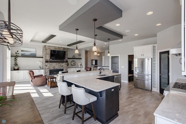 kitchen with white cabinets, pendant lighting, a stone fireplace, a large island with sink, and stainless steel appliances