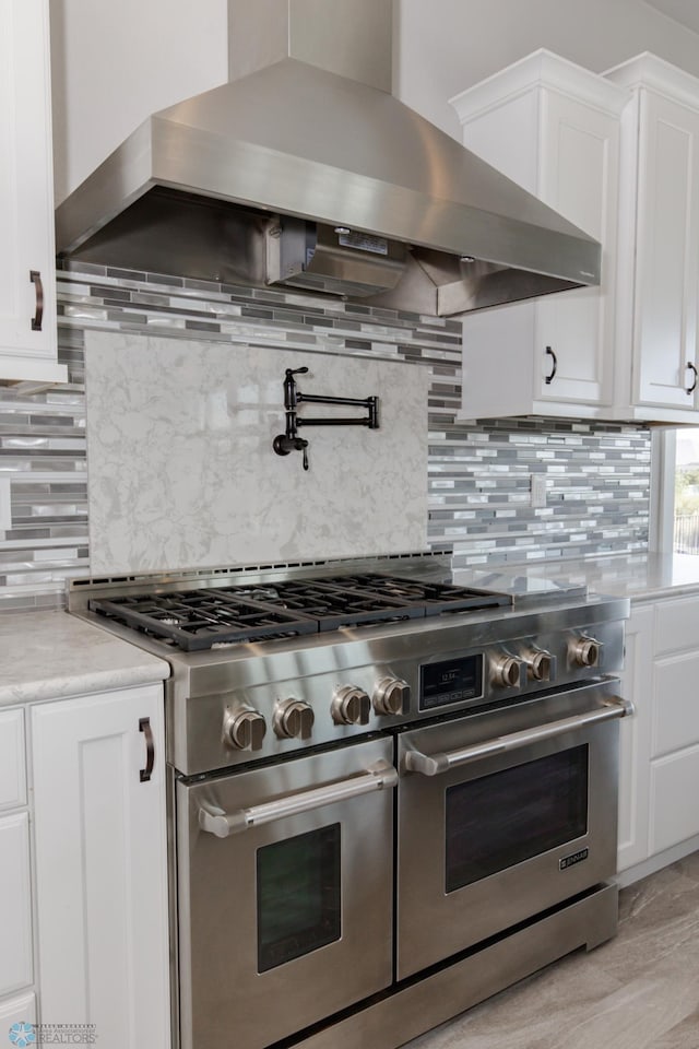 kitchen with range with two ovens, wall chimney exhaust hood, tasteful backsplash, and white cabinetry