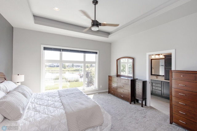 carpeted bedroom with a raised ceiling, ceiling fan, and ensuite bath