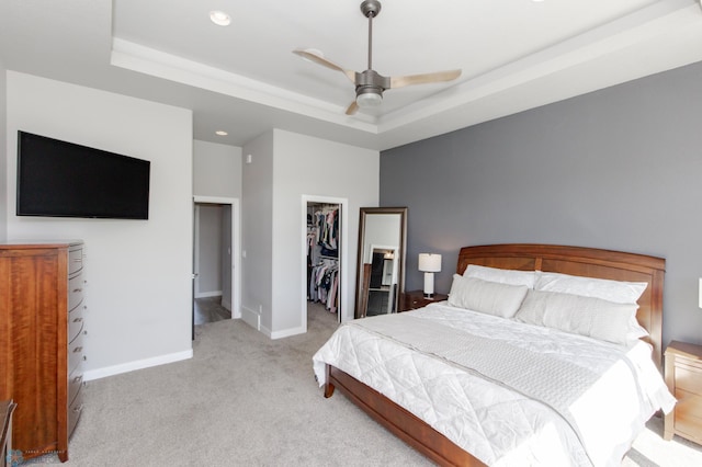 bedroom featuring ceiling fan, a raised ceiling, a walk in closet, a closet, and light colored carpet