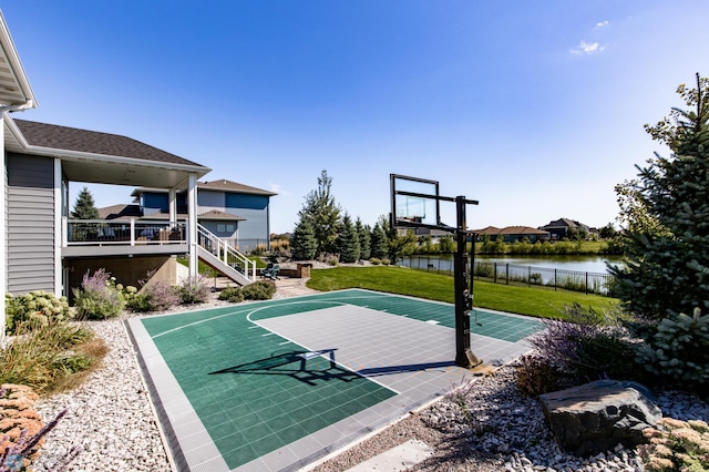 view of sport court with a water view and a lawn