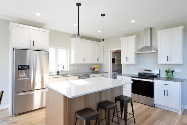 kitchen featuring white cabinets, appliances with stainless steel finishes, wall chimney range hood, and a center island