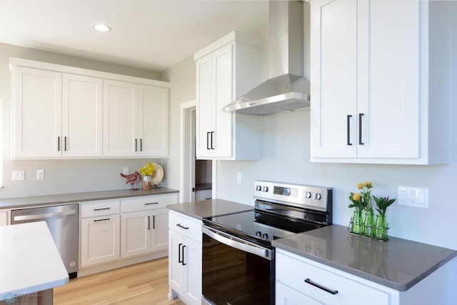 kitchen featuring appliances with stainless steel finishes, wall chimney exhaust hood, light hardwood / wood-style flooring, and white cabinets