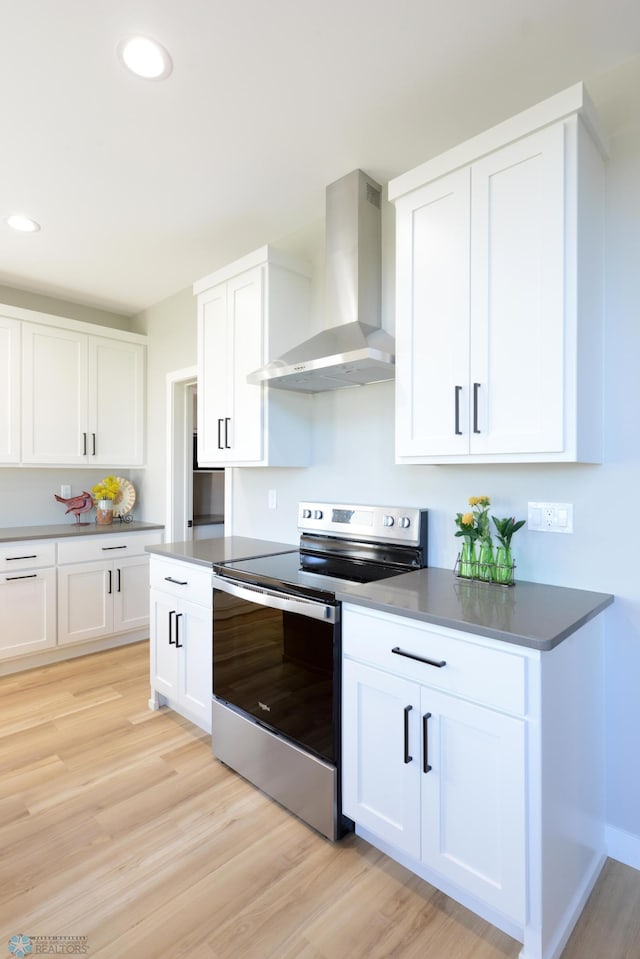 kitchen featuring light wood-type flooring, wall chimney range hood, white cabinetry, and electric range