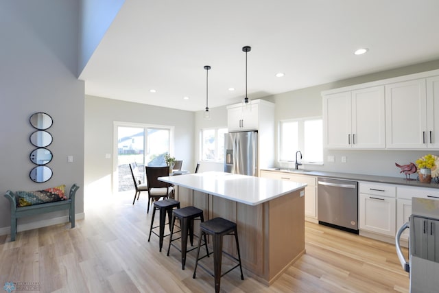 kitchen with light hardwood / wood-style floors, a center island, white cabinets, stainless steel appliances, and decorative light fixtures