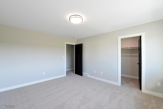 unfurnished bedroom with light carpet, a walk in closet, and a closet