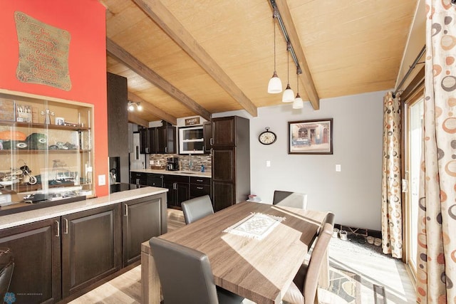 dining space featuring light wood-type flooring, lofted ceiling with beams, and sink