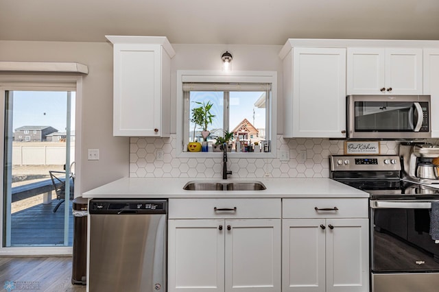 kitchen with wood-type flooring, sink, white cabinetry, backsplash, and appliances with stainless steel finishes