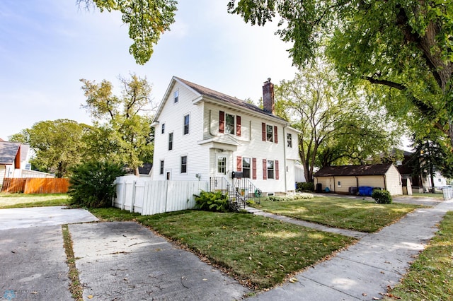 colonial-style house featuring a garage, a front yard, and an outbuilding