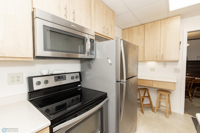 kitchen with a paneled ceiling, light brown cabinets, and stainless steel appliances