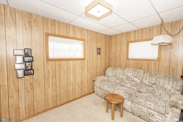 living area featuring a drop ceiling, wood walls, and carpet flooring