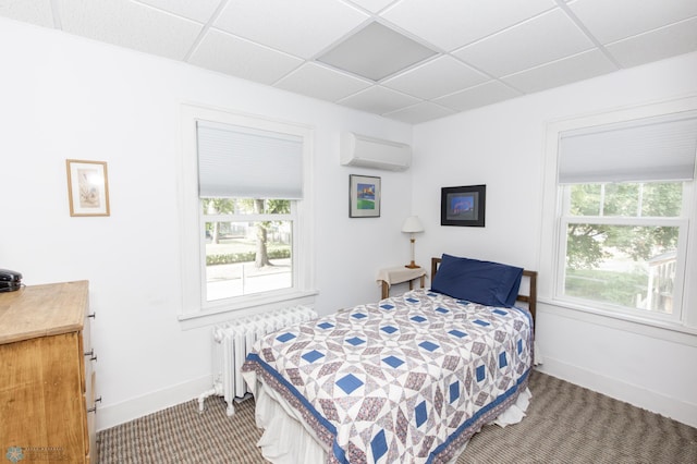 carpeted bedroom with an AC wall unit, radiator, and a paneled ceiling