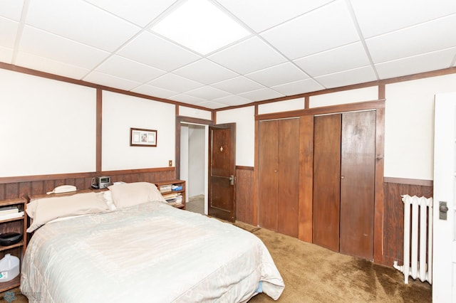 bedroom featuring carpet floors, a closet, radiator, a paneled ceiling, and wooden walls