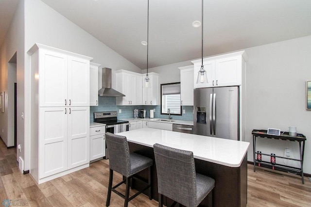 kitchen featuring pendant lighting, wall chimney exhaust hood, appliances with stainless steel finishes, a center island, and light wood-type flooring