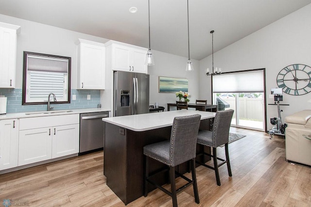 kitchen featuring hanging light fixtures, light hardwood / wood-style floors, vaulted ceiling, white cabinets, and stainless steel appliances