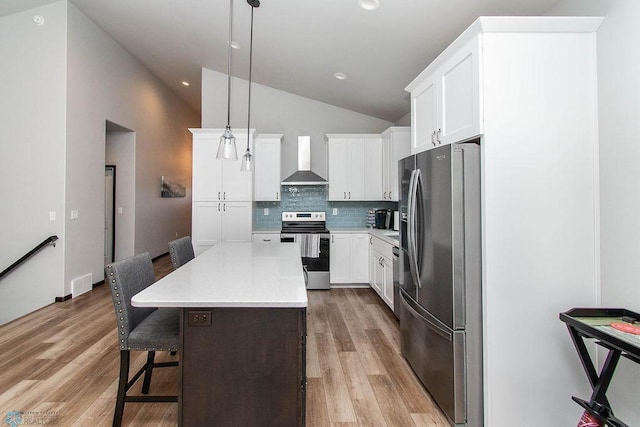 kitchen featuring appliances with stainless steel finishes, white cabinetry, wall chimney exhaust hood, a center island, and decorative light fixtures