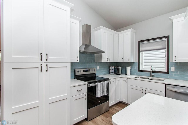 kitchen featuring appliances with stainless steel finishes, white cabinetry, sink, and wall chimney range hood