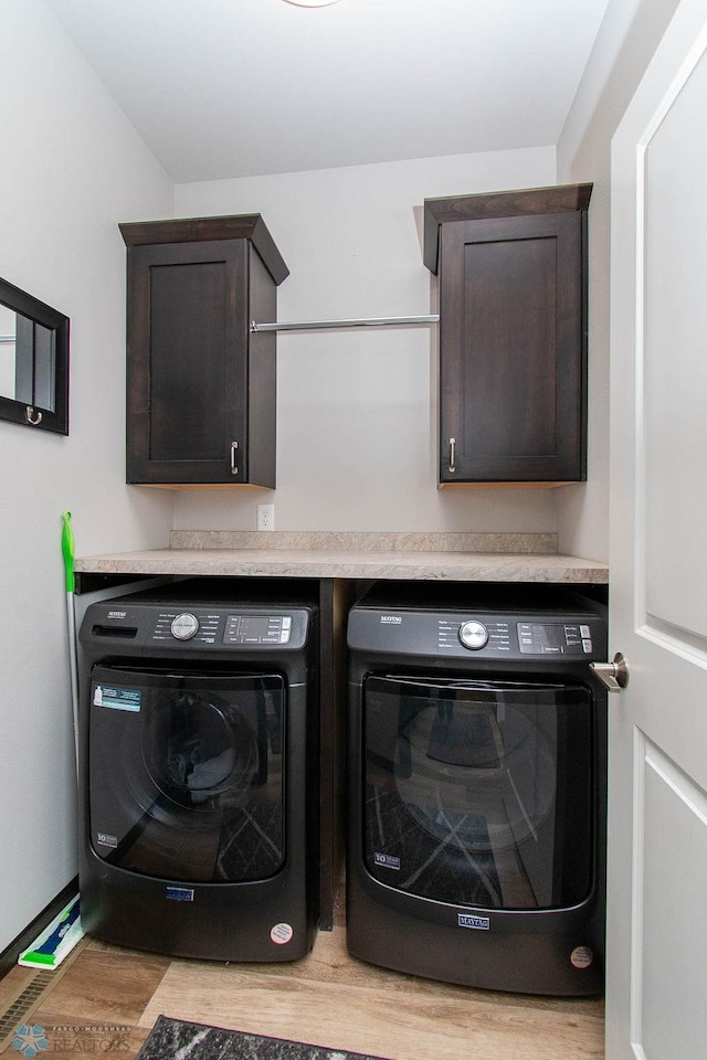 laundry room featuring light hardwood / wood-style floors, separate washer and dryer, and cabinets