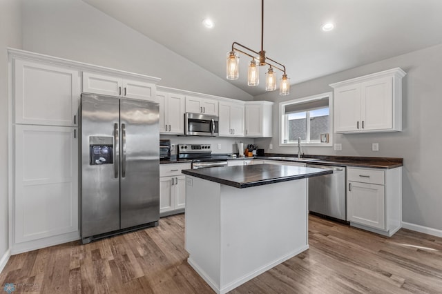 kitchen featuring white cabinets, stainless steel appliances, hanging light fixtures, and lofted ceiling