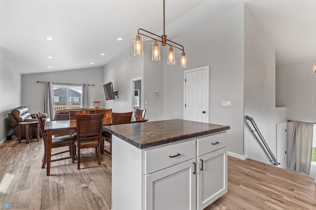 kitchen featuring light hardwood / wood-style floors, vaulted ceiling, white cabinets, a center island, and decorative light fixtures