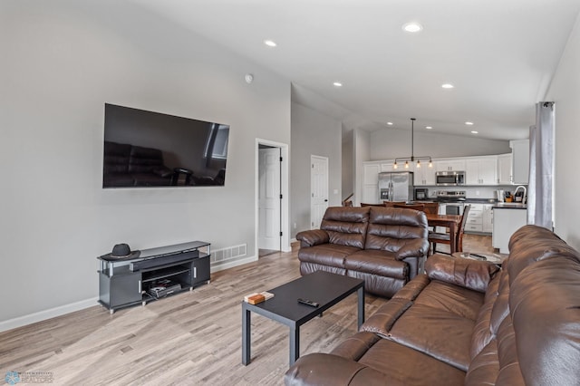 living room with light wood-type flooring, sink, and high vaulted ceiling