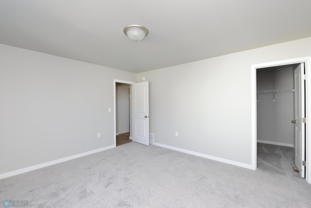 unfurnished bedroom featuring light carpet, a walk in closet, and a closet