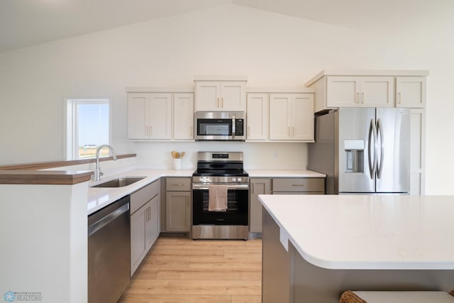 kitchen featuring stainless steel appliances, vaulted ceiling, light wood-type flooring, and sink