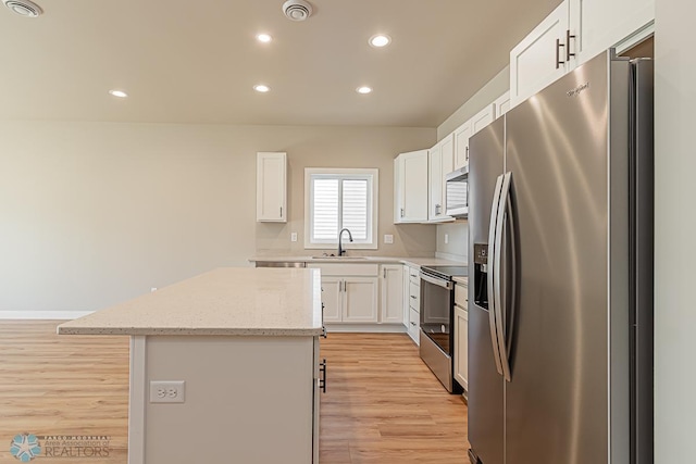 kitchen with white cabinets, light stone countertops, stainless steel appliances, light wood-type flooring, and a center island