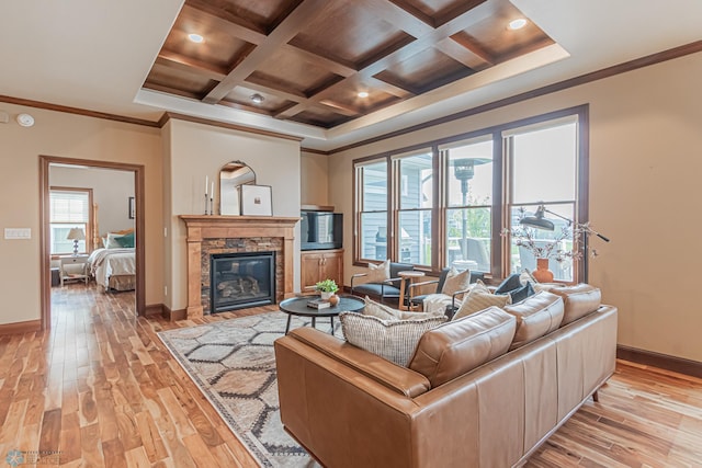 living room featuring coffered ceiling, a stone fireplace, beamed ceiling, light wood-type flooring, and ornamental molding