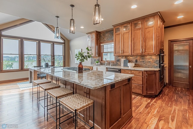 kitchen with appliances with stainless steel finishes, vaulted ceiling, pendant lighting, a center island, and light hardwood / wood-style flooring